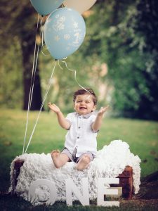 Glad bebis klappar händer och sitter på koffert i parken med ballonger