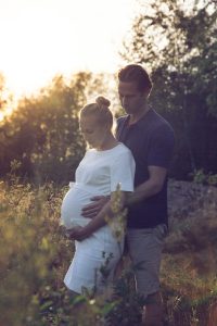 Gravidfoto i Önnered, solen går ner och paret tittar ner på magen